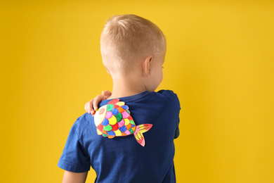 Photo of Little boy with paper fish on back against yellow background. April fool's day