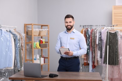 Dry-cleaning service. Happy worker with notebook in workplace indoors