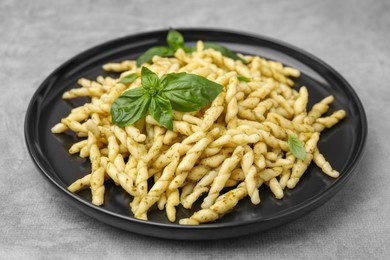 Plate of delicious trofie pasta with pesto sauce and basil leaves on light grey table