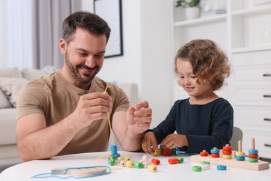Motor skills development. Father and daughter playing with wooden pieces and strings for threading activity at table indoors