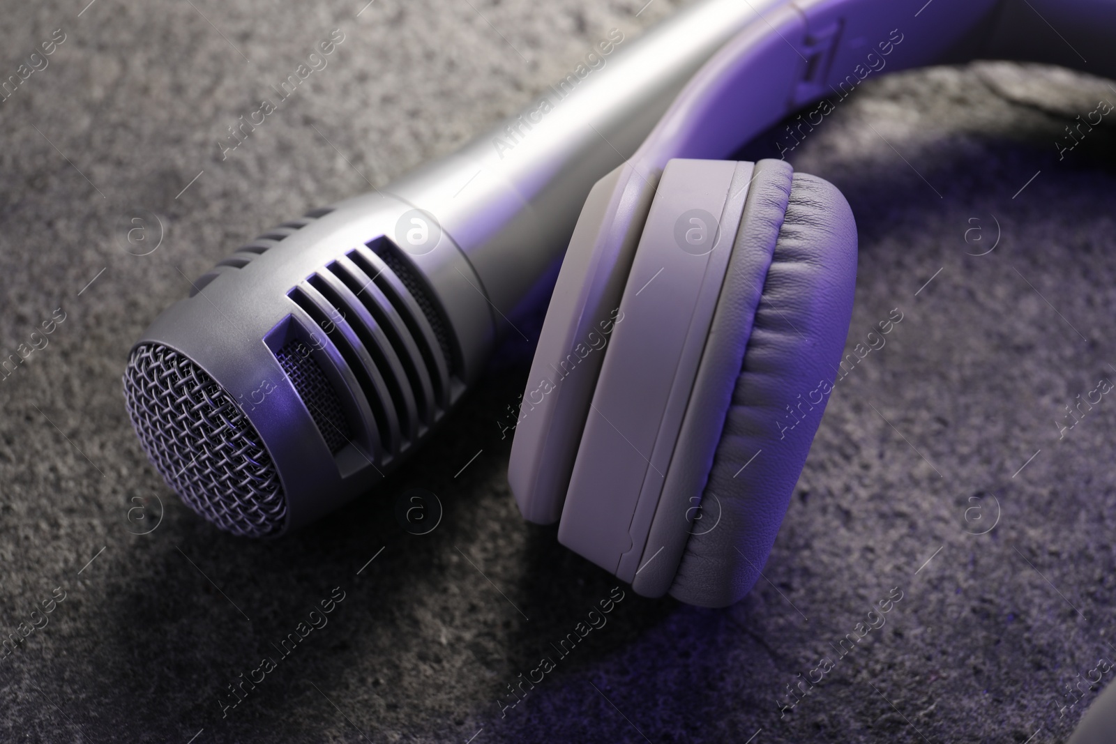 Photo of Microphone and headphones on grey textured table, closeup. Sound recording and reinforcement
