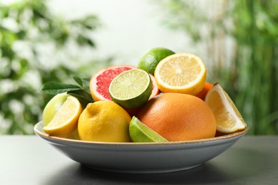 Photo of Different fresh citrus fruits and leaves on grey table against blurred background, closeup