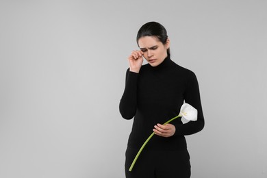 Photo of Sad woman with calla lily flower mourning on light grey background, space for text. Funeral ceremony