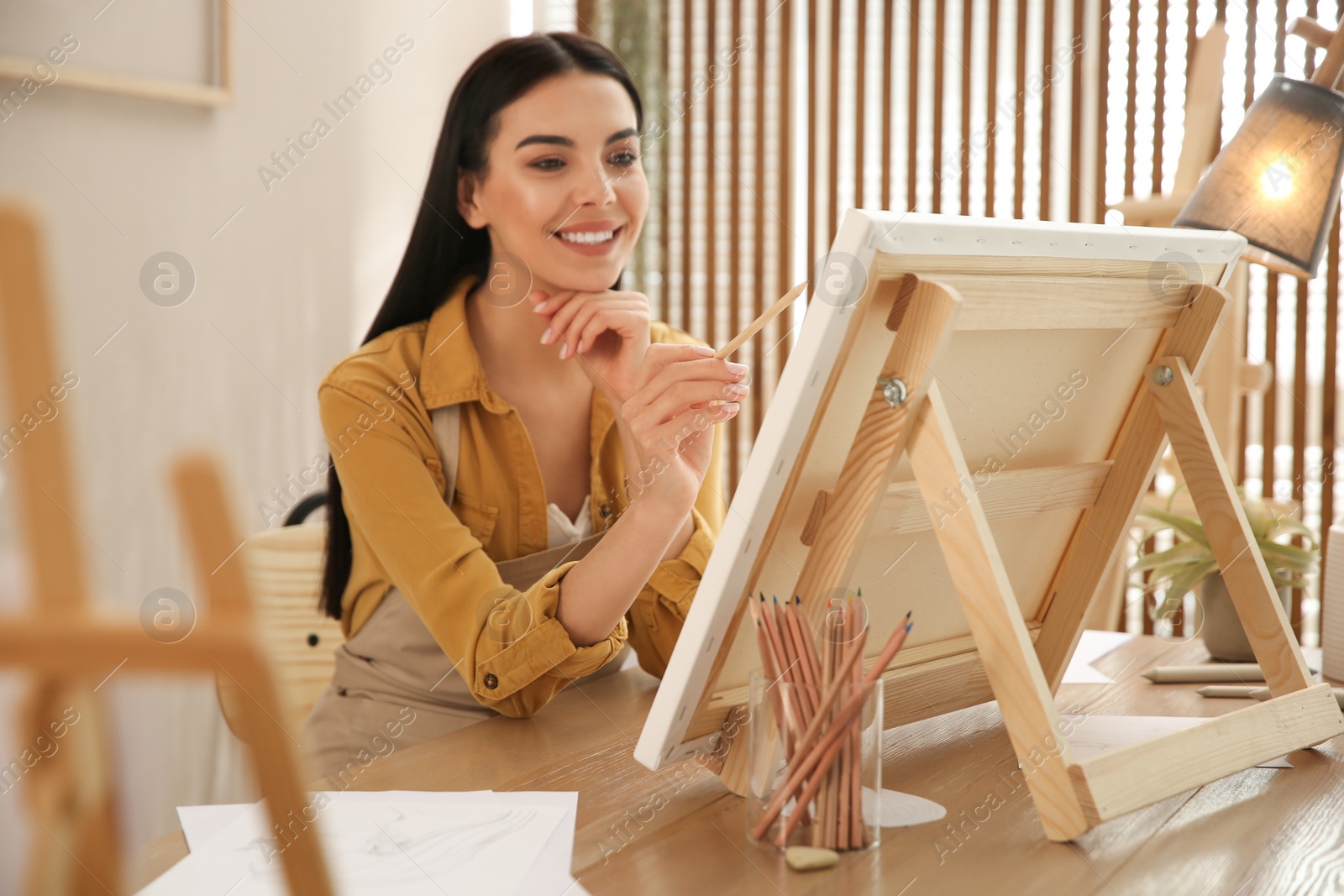 Photo of Young woman drawing on easel with pencil at table indoors