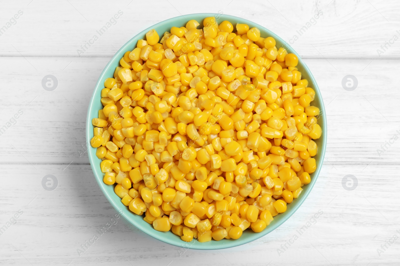 Photo of Delicious canned corn in bowl on white wooden table, top view