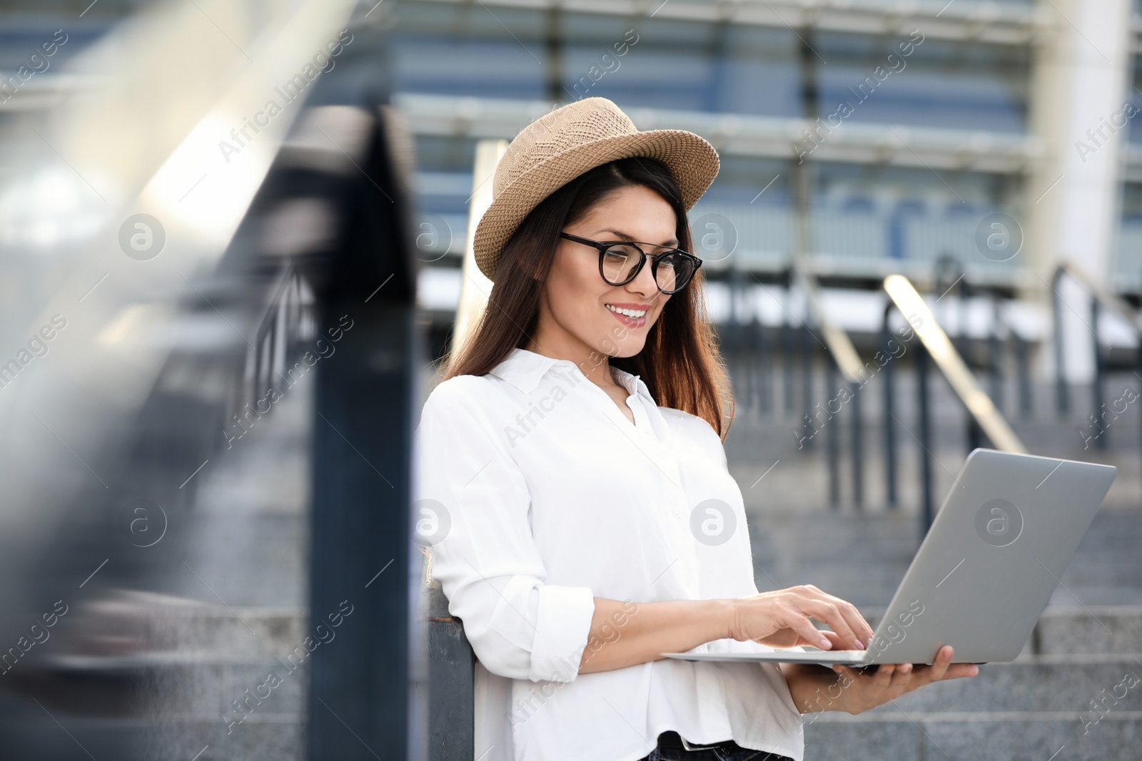 Photo of Beautiful woman with glasses using laptop on city street