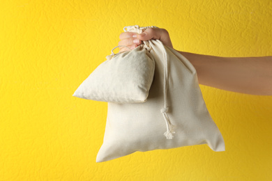 Photo of Woman holding full cotton eco bags on yellow background, closeup