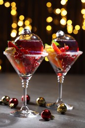 Photo of Creative presentation of Christmas Sangria cocktail in baubles and glasses on grey table against black background with blurred lights