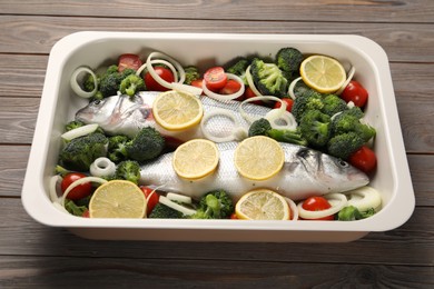 Photo of Raw fish with vegetables and lemon in baking dish on wooden table