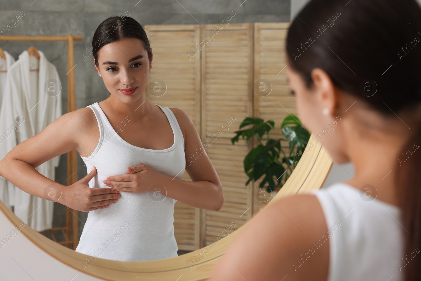 Photo of Beautiful young woman doing breast self-examination near mirror in bathroom