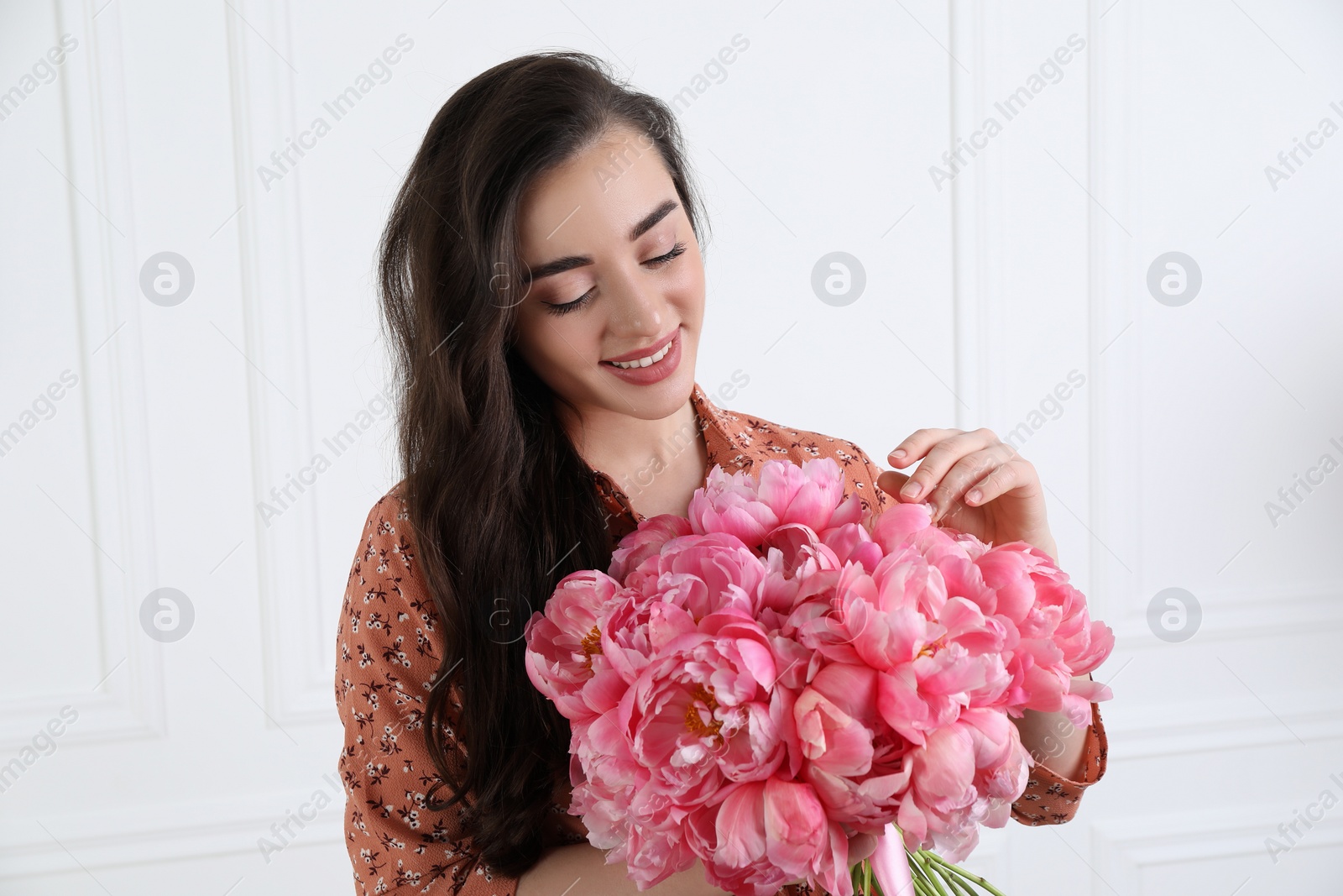 Photo of Beautiful young woman with bouquet of pink peonies near white wall