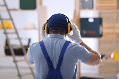 Photo of Worker wearing safety headphones indoors, back view. Hearing protection device