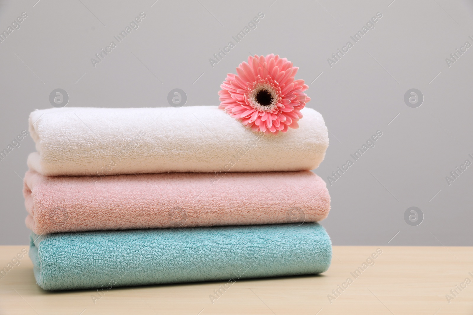 Photo of Stack of fresh towels with flower on table