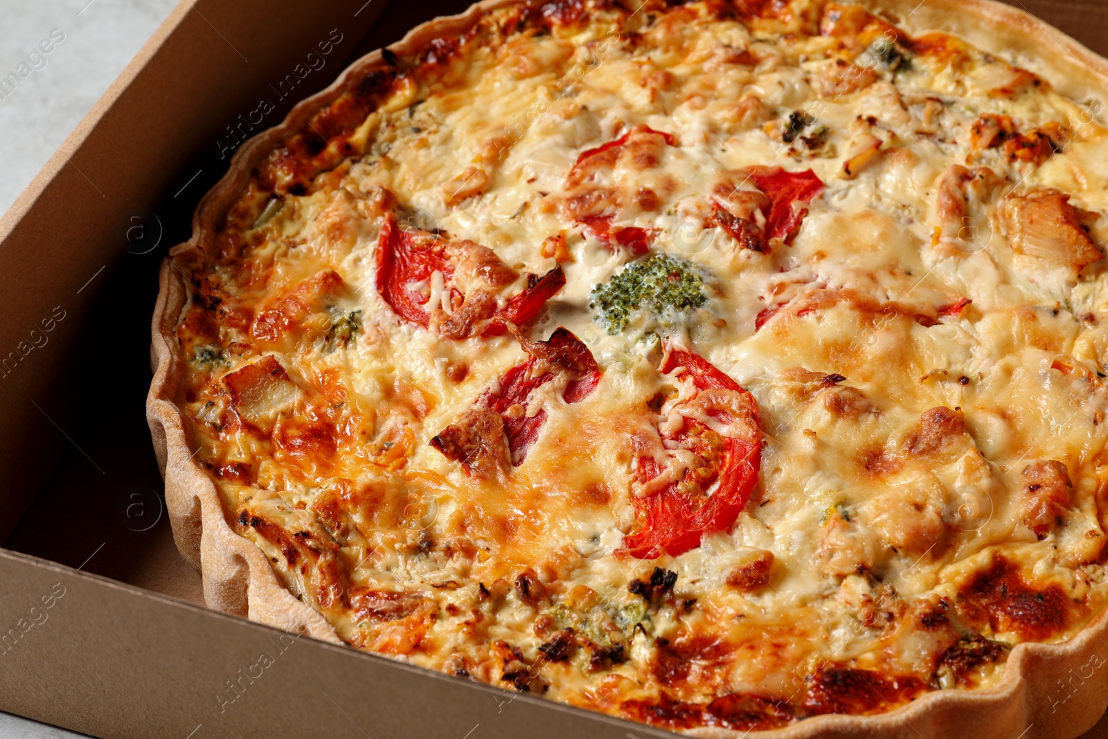 Photo of Tasty quiche with tomatoes and cheese in open box on table, closeup