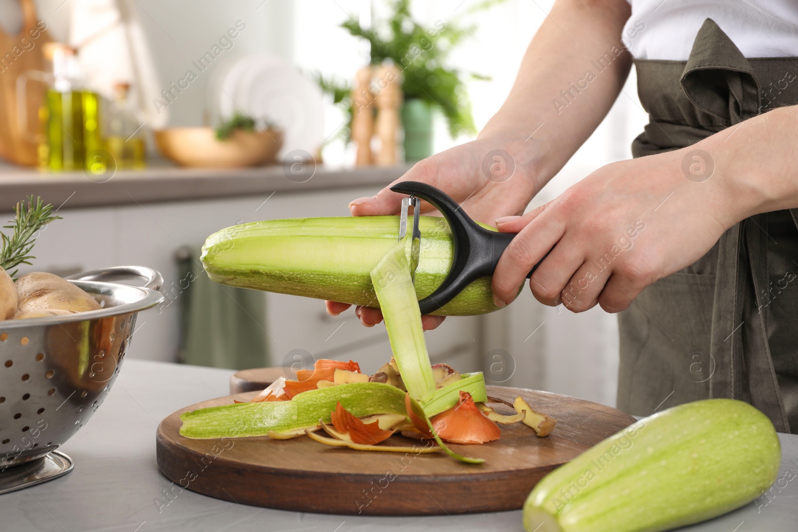 Photo of Woman peeling fresh zucchini at light table indoors, closeup