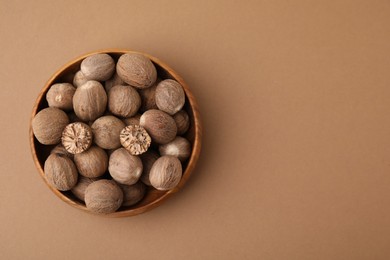 Photo of Nutmegs in wooden bowl on light brown background, top view. Space for text