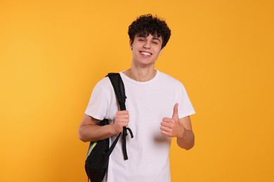 Photo of Handsome young man with backpack showing thumb up on orange background