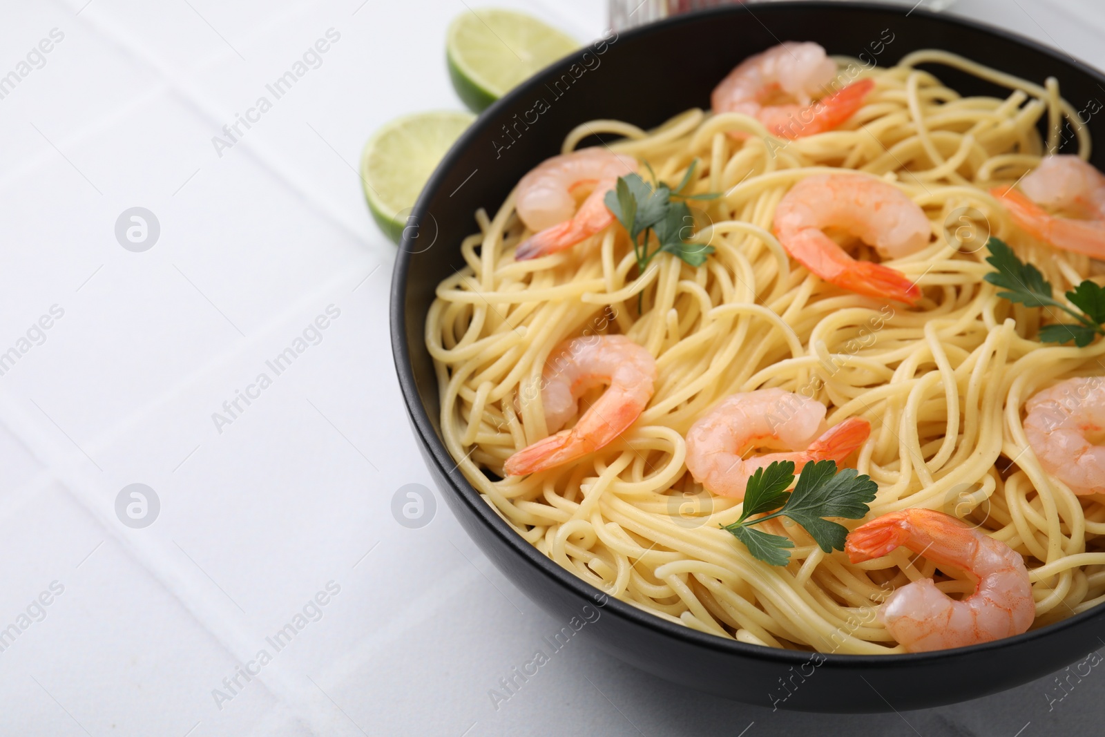 Photo of Tasty spaghetti with shrimps and parsley in bowl on light tiled table, closeup. Space for text