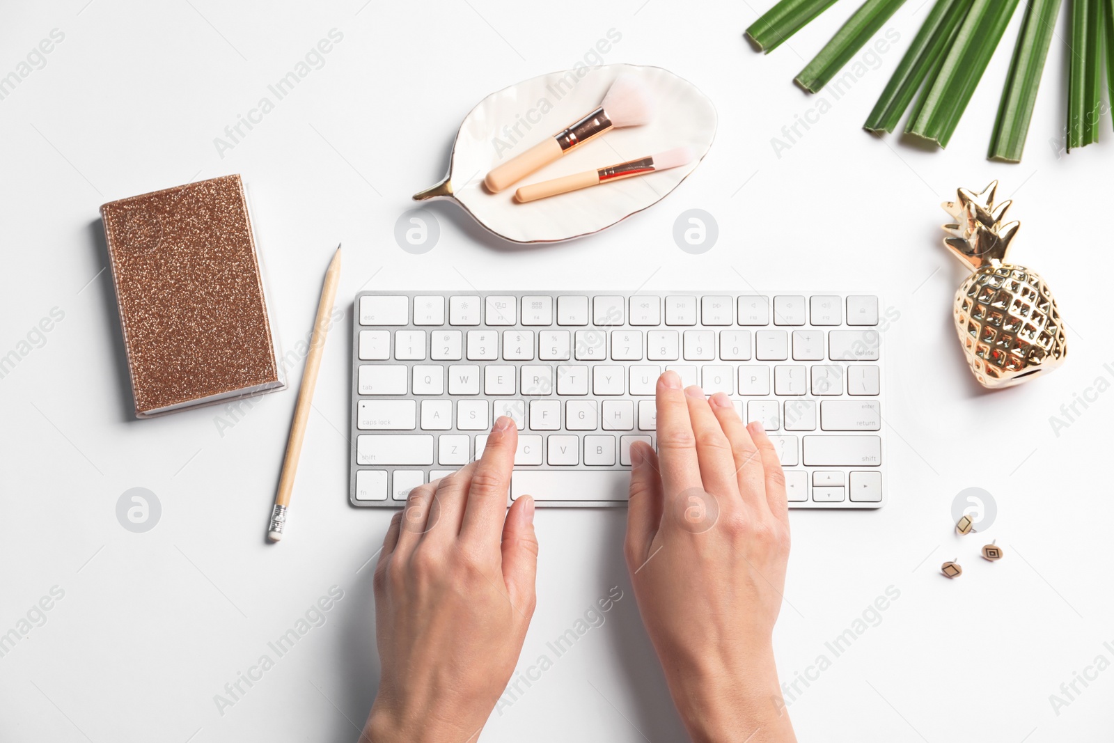 Photo of Woman using computer keyboard on white table decorated with tropical leaf, top view. Creative design ideas