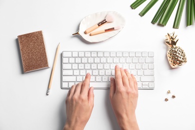 Photo of Woman using computer keyboard on white table decorated with tropical leaf, top view. Creative design ideas