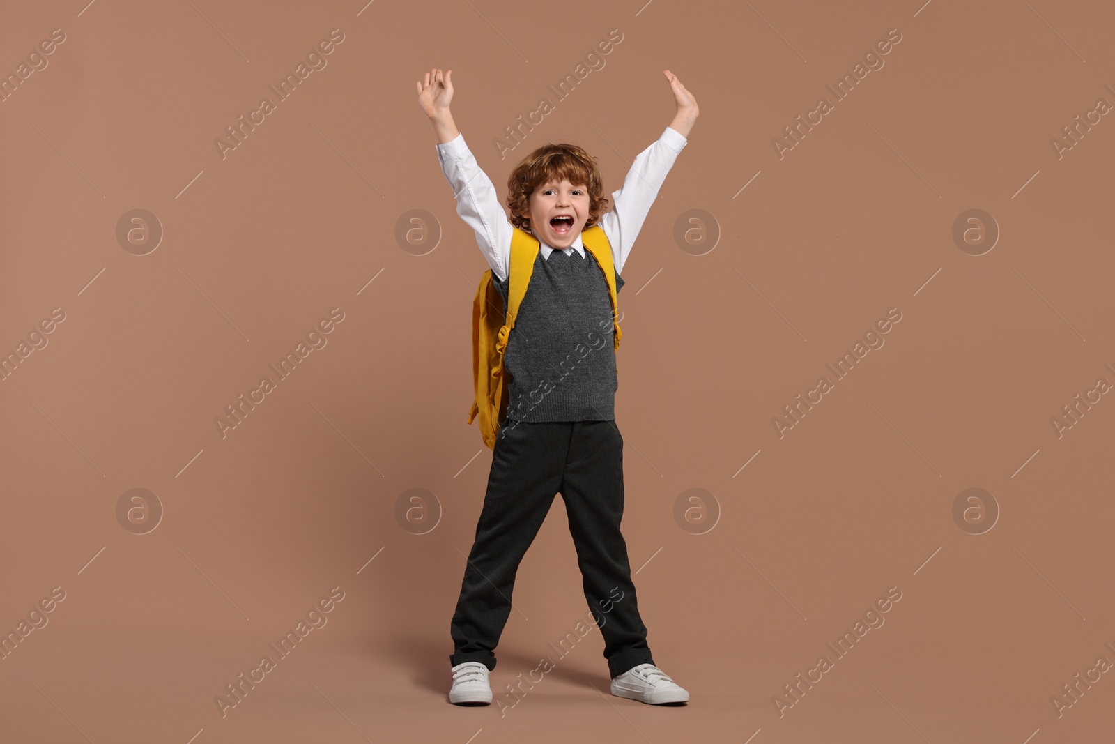 Photo of Emotional schoolboy with backpack on brown background