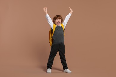 Emotional schoolboy with backpack on brown background