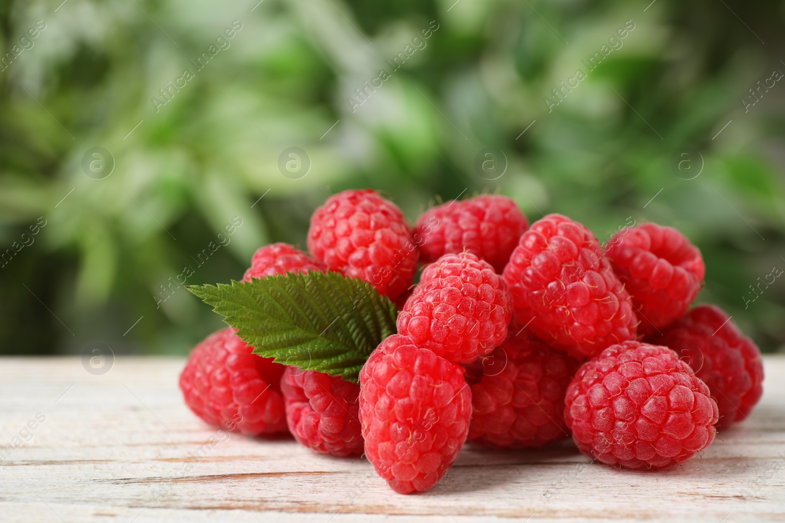 Photo of Delicious fresh ripe raspberries with green leaf on white wooden table