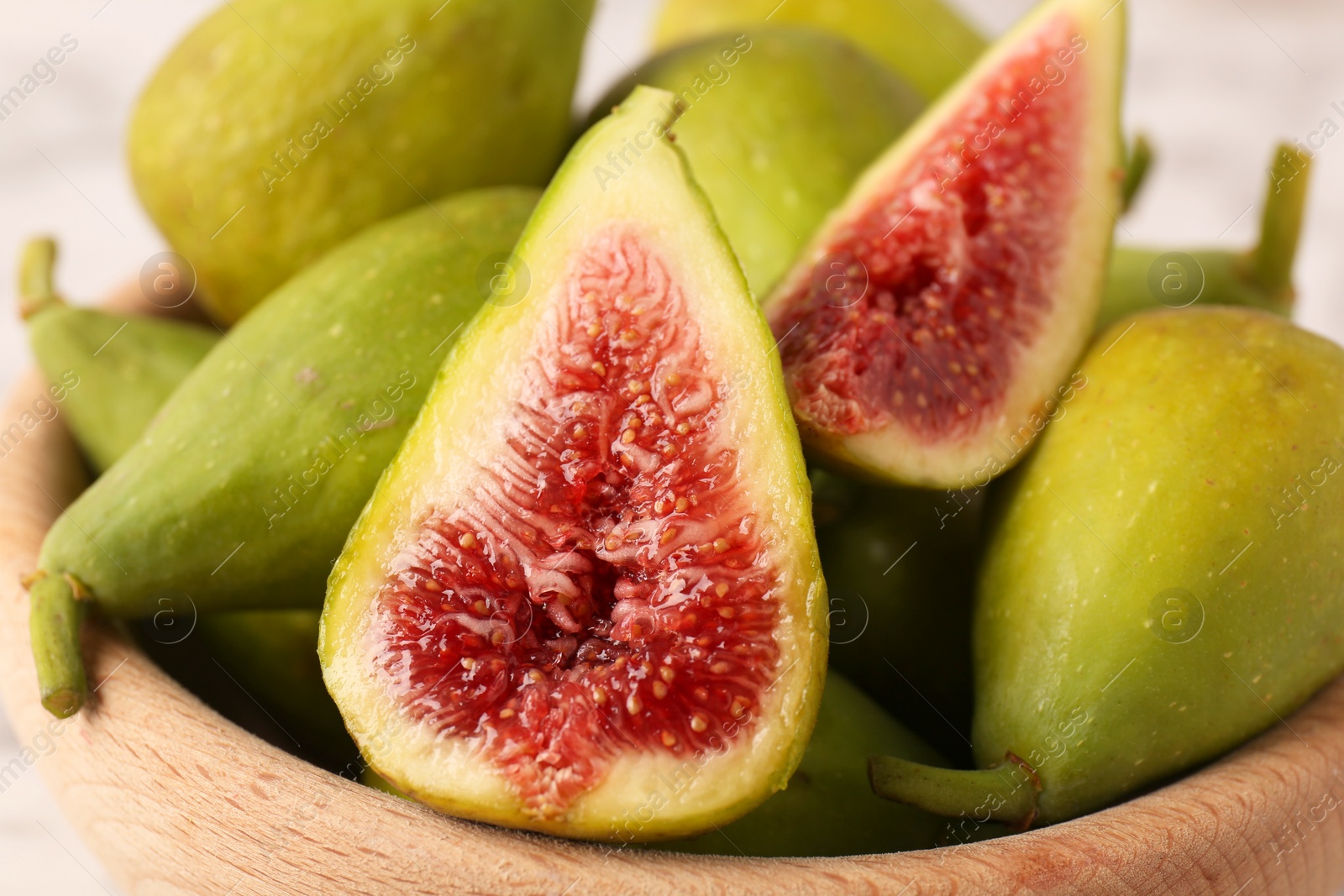 Photo of Cut and whole green figs in bowl, closeup