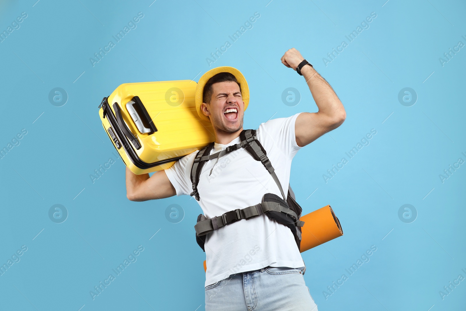 Photo of Emotional male tourist with travel backpack and suitcase on turquoise background