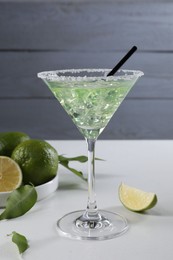 Delicious Margarita cocktail with ice cubes in glass and lime on white table