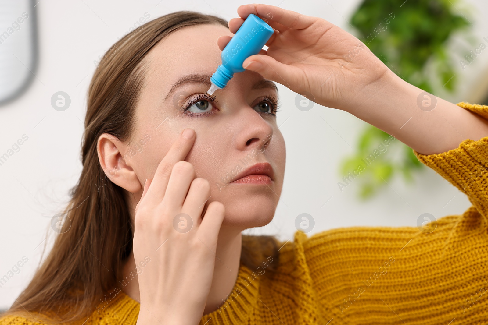 Photo of Young woman applying medical eye drops indoors, closeup