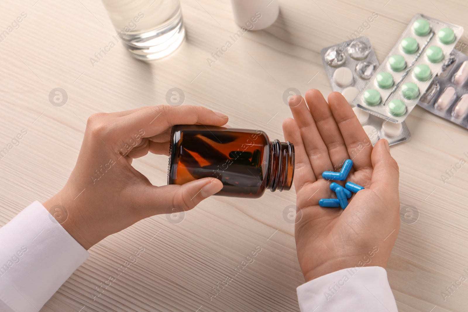 Photo of Woman taking out of bottle pills at white wooden table, closeup