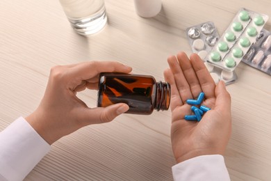 Woman taking out of bottle pills at white wooden table, closeup