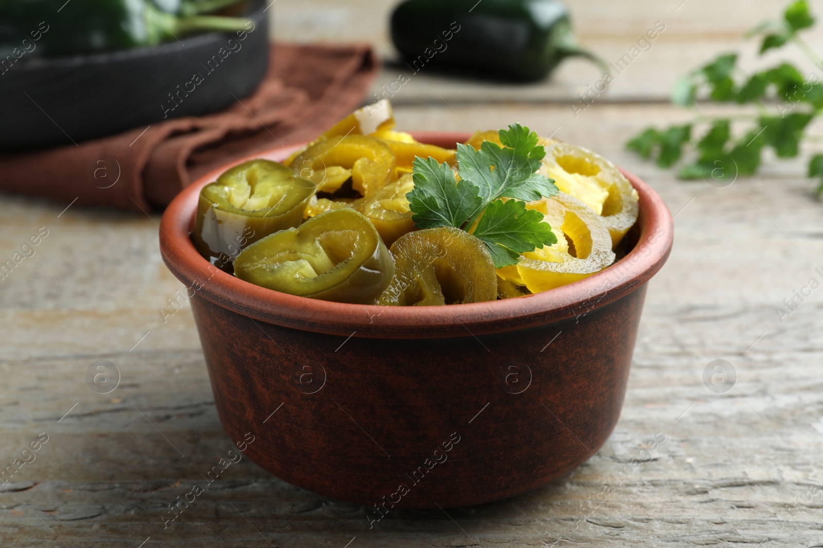 Photo of Bowl with slices of pickled green jalapeno peppers on wooden table