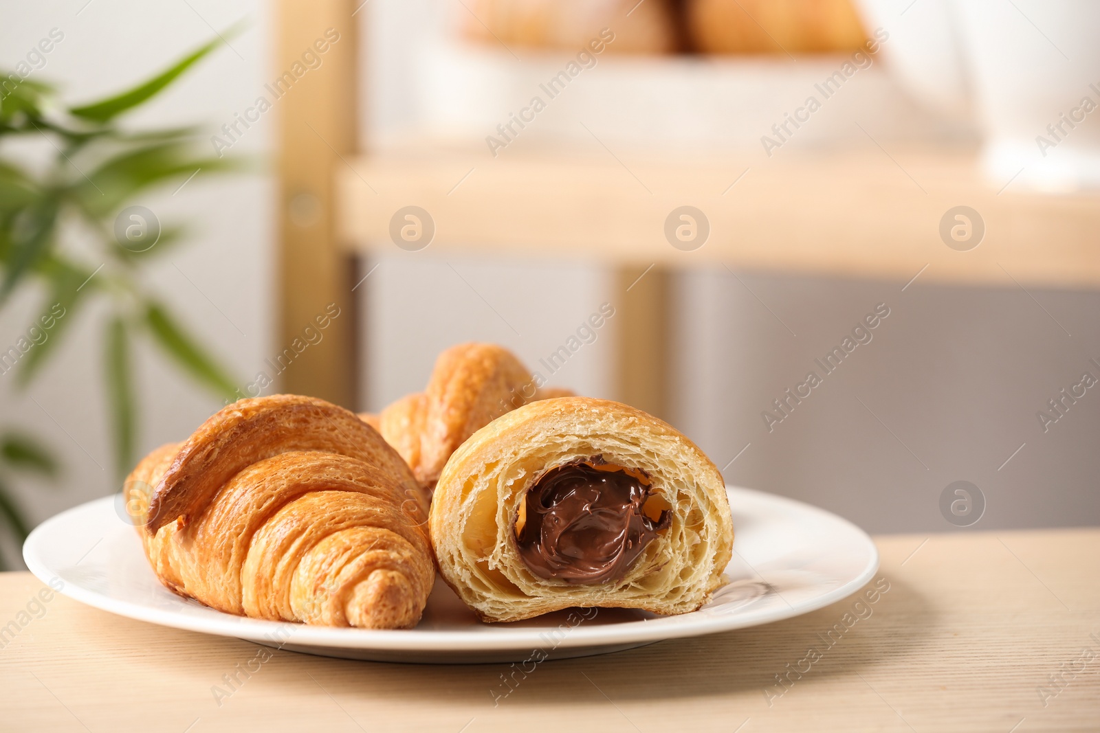 Photo of Plate of fresh croissants with chocolate stuffing on wooden table indoors. French pastry