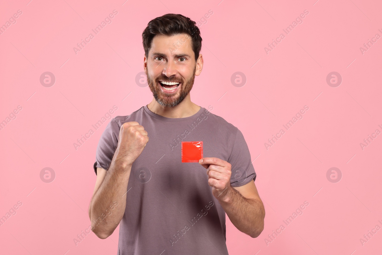 Photo of Emotional man holding condom on pink background. Safe sex