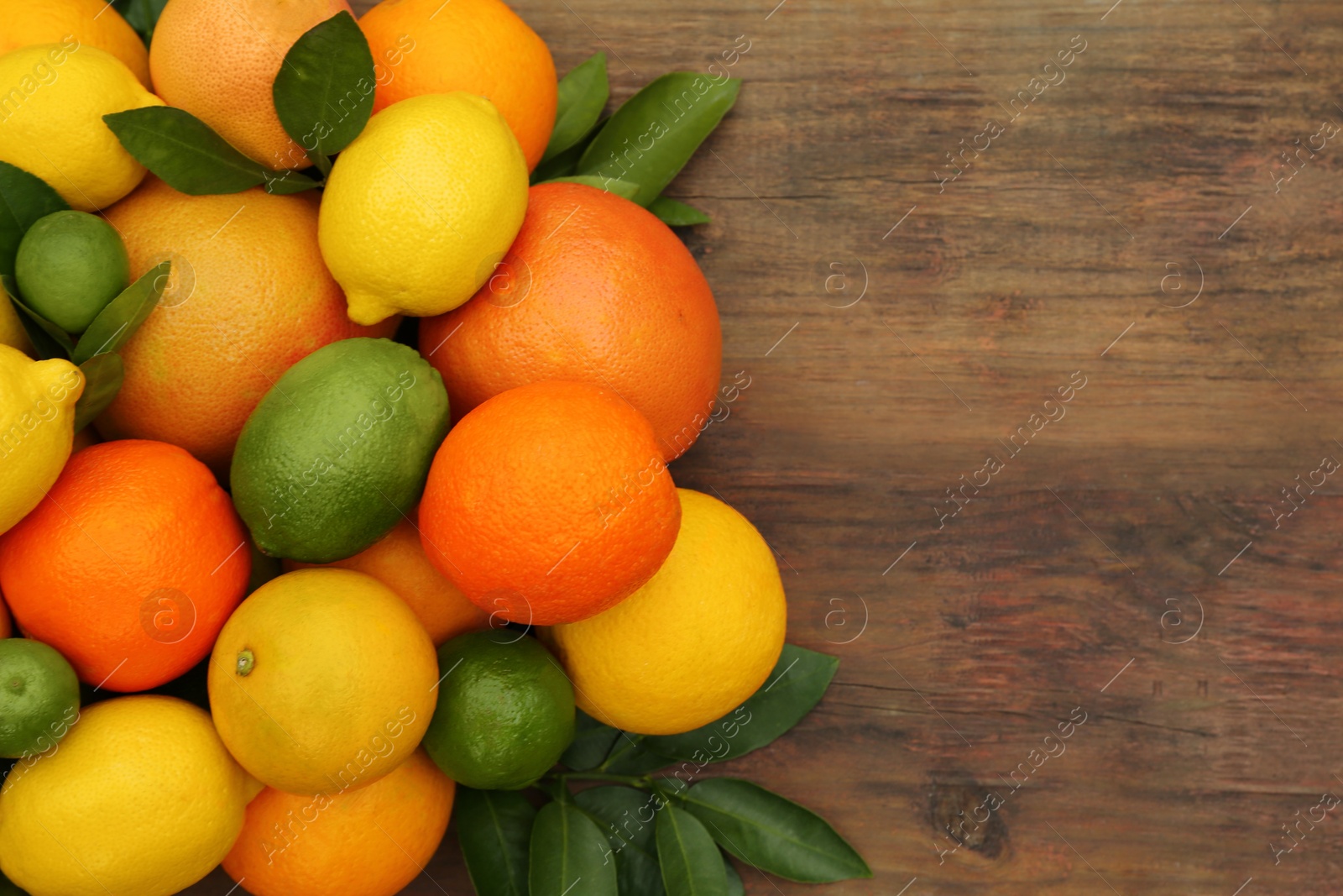 Photo of Different citrus fruits with green leaves on wooden table, flat lay. Space for text