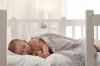 Photo of Cute little baby with toy bear sleeping in soft crib at home