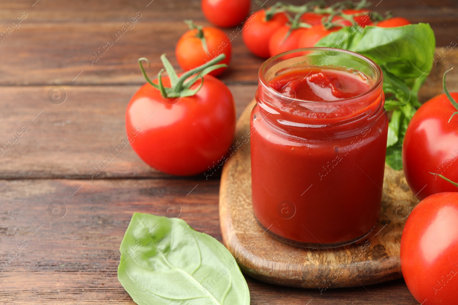 Photo of Jar of tasty ketchup and tomatoes on wooden table, closeup. Space for text