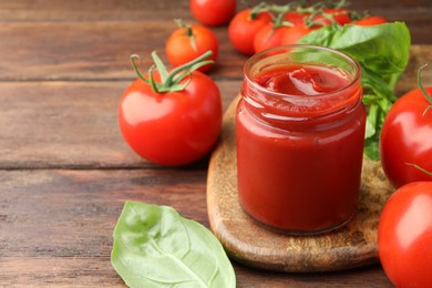 Photo of Jar of tasty ketchup and tomatoes on wooden table, closeup. Space for text