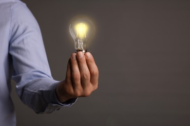 Photo of Glow up your ideas. Closeup view of man holding light bulb on grey background, space for text
