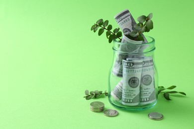 Photo of Financial savings. Dollar banknotes in glass jar, twigs and coins on green background