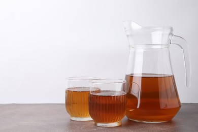 Photo of Homemade fermented kombucha in glasses and jug on grey table. Space for text