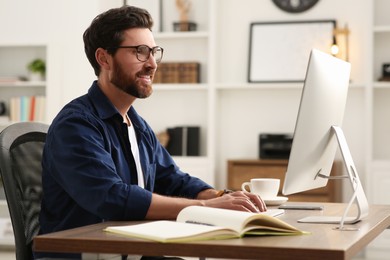 Home workplace. Happy man working with computer at wooden desk in room