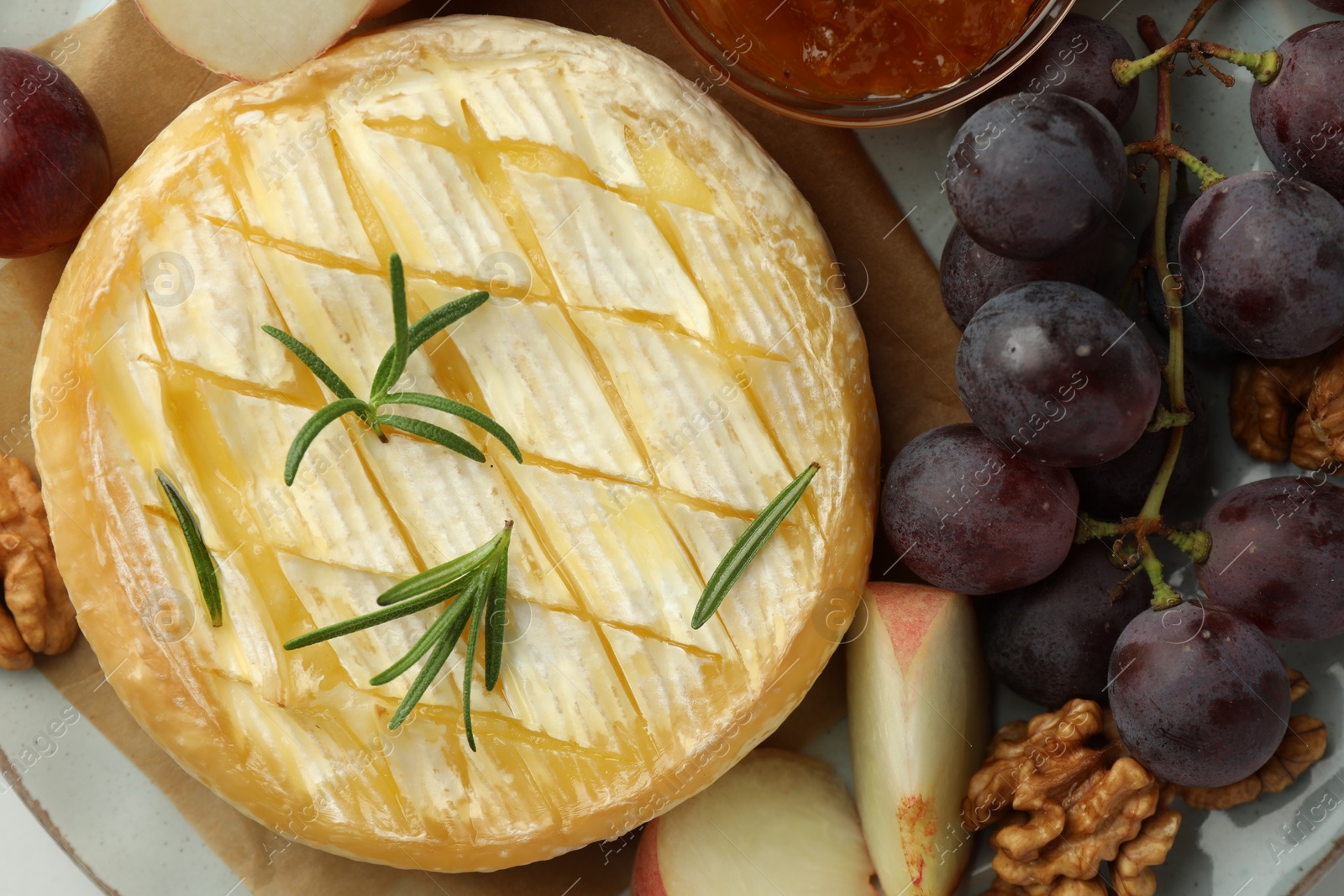 Photo of Tasty baked brie cheese with rosemary, fruits and walnuts on plate, top view