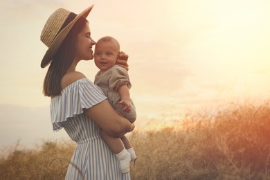 Happy mother with adorable baby in field at sunset, space for text