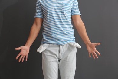 Man showing empty pockets on grey background, closeup