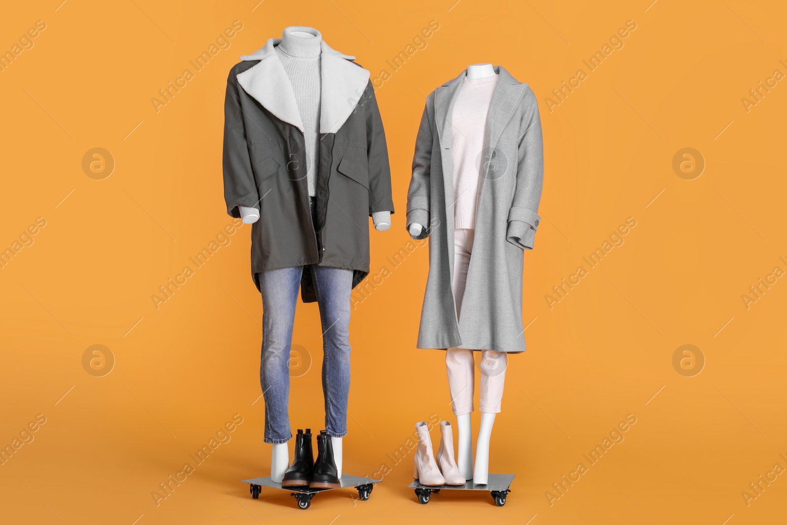 Photo of Mannequins with boots dressed in stylish coat, jacket, sweater and turtleneck on orange background