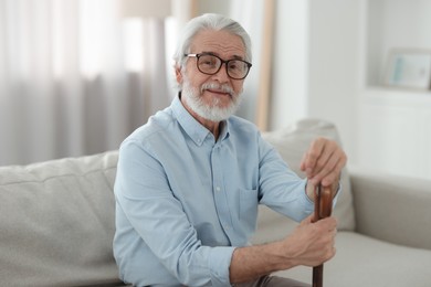 Portrait of grandpa with glasses and walking cane on sofa indoors