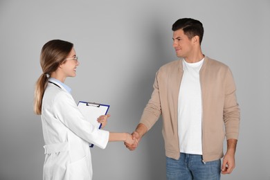 Photo of Doctor and patient shaking hands on light grey background